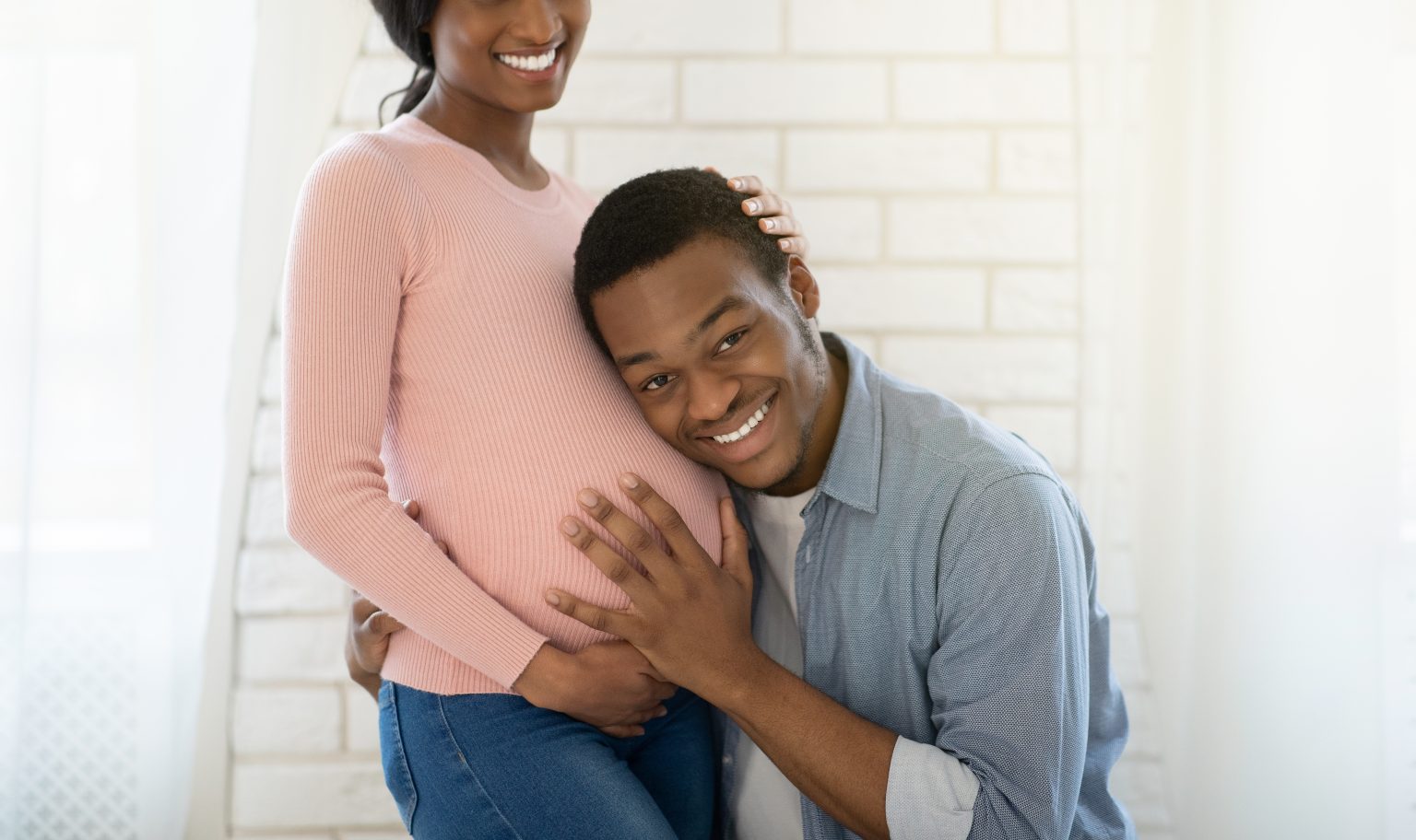 Loving black guy listening his girlfriend's pregnant tummy at home, panorama. Happy future father embracing his expectant wife and putting ear to her belly, feeling excited indoors